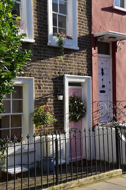 A close-up view of a charming townhouse in Covent Garden featuring a pink front door decorated with a lush green wreath and surrounded by white window frames with flower boxes containing vibrant pink